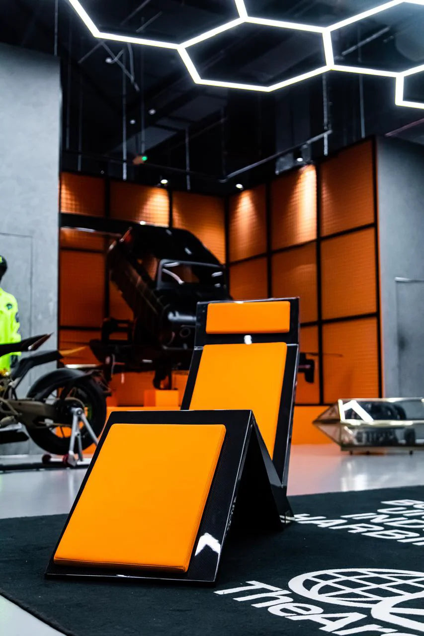 Orange-and-black automotive display showroom with motorcycles and vehicle exhibits under geometric ceiling lights