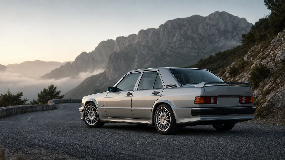Silver-gray 1980s performance sedan with subtle aerodynamic bodywork on a mountain road.