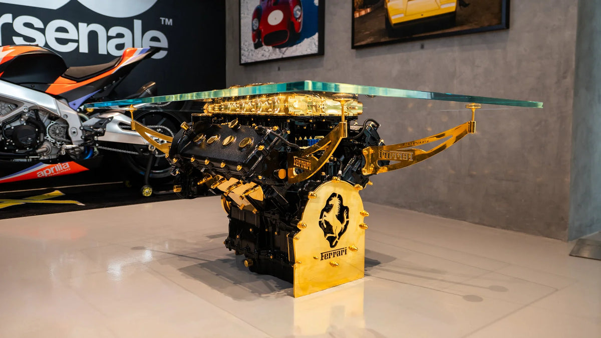 Black and gold automotive engine displayed on a gold-toned pedestal beneath a transparent canopy in a showroom.