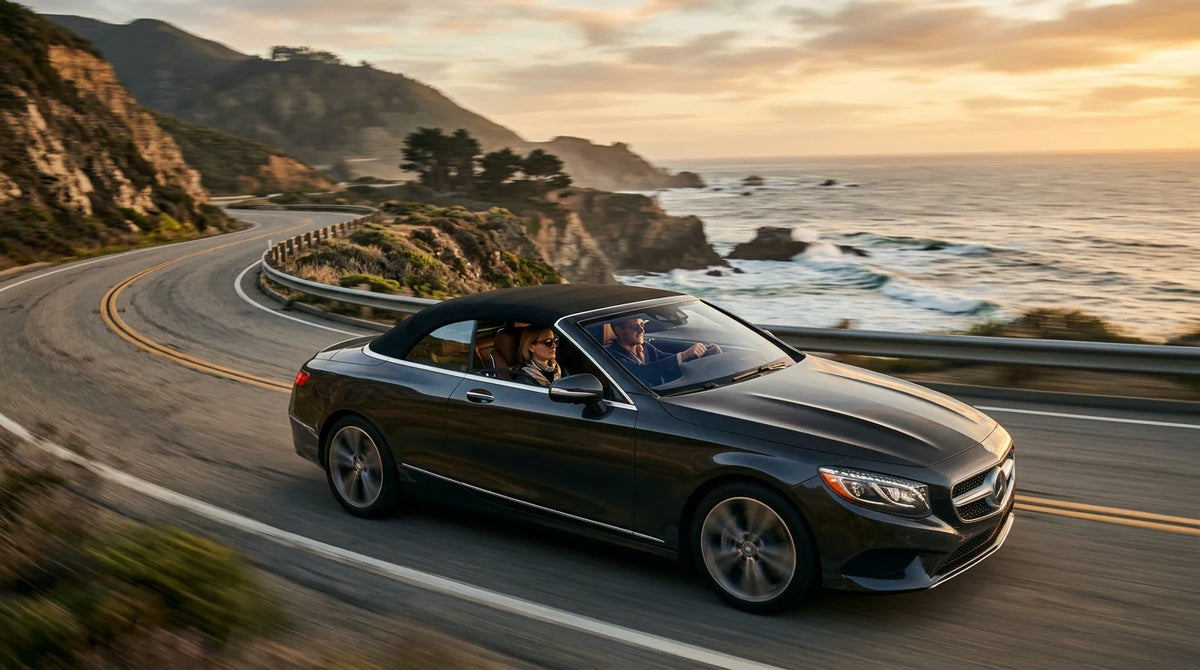 Luxury convertible driving with the top down on a scenic coastal road at sunset