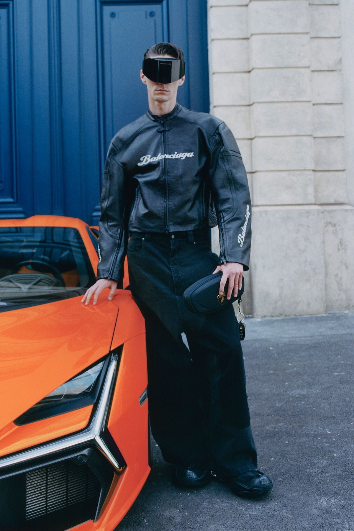 Balenciaga | Automobili Lamborghini Fall 25 campaign image: a model in a leather racing jacket beside a Lamborghini Revuelto